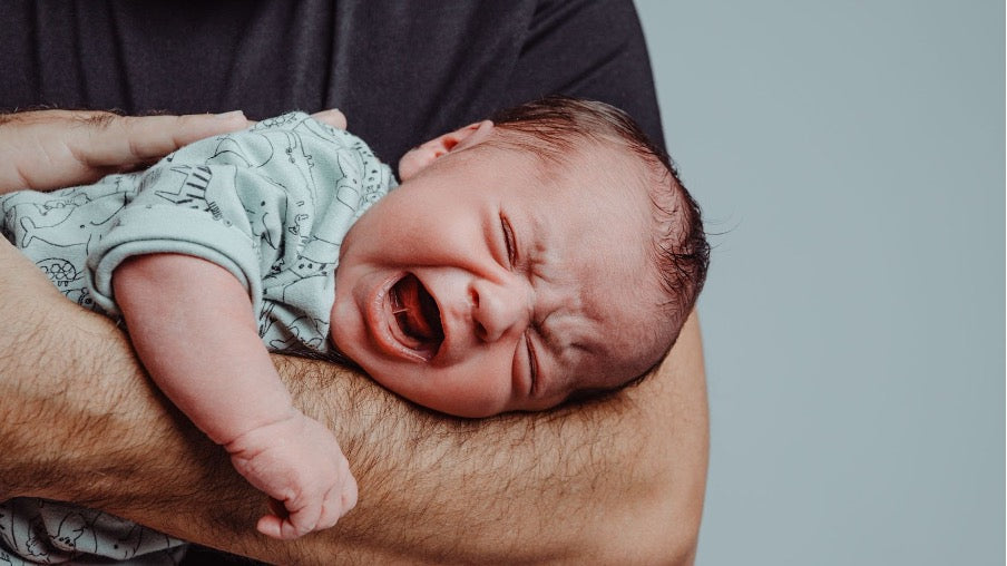 A baby with colic symptoms crying whilst being held in their father’s arms.   A baby with colic symptoms crying whilst being held in their father’s arms.