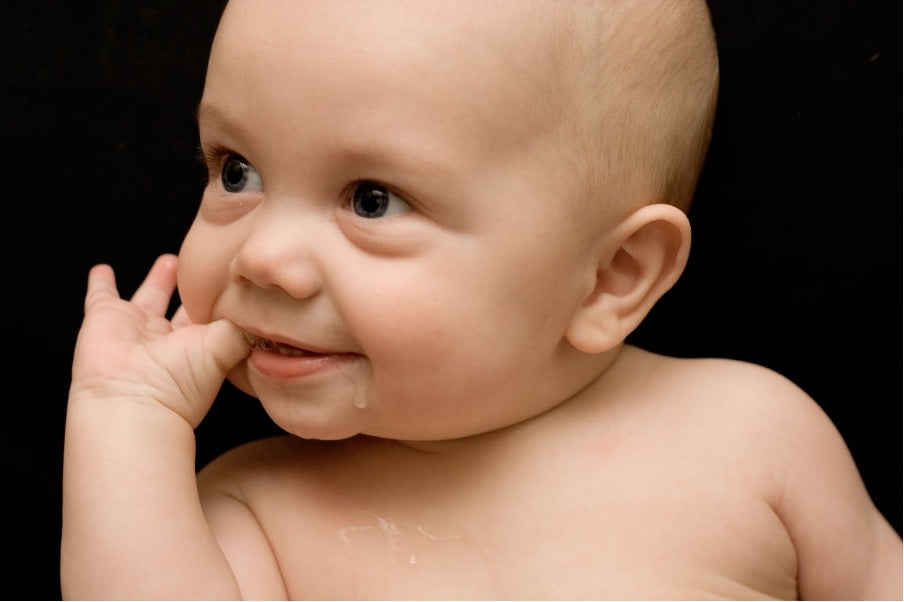  An image of a baby dribbling. Its fingers are in its mouth. 