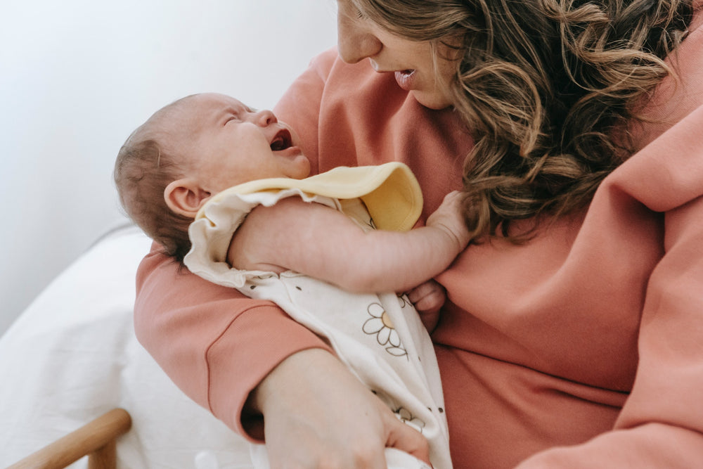  a newborn baby crying whilst being held by their mother. 
