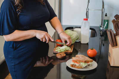 A pregnant woman prepares a healthy, nutritious meal, including salad which is good food for pregnant women.